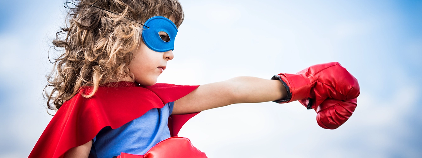 young girl in superhero costume punches the air signifying her strength and her fight to learn to read.
