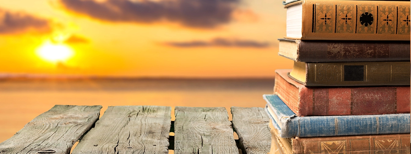 A stack of books sits on a dock overlooking a body of water at sunset.