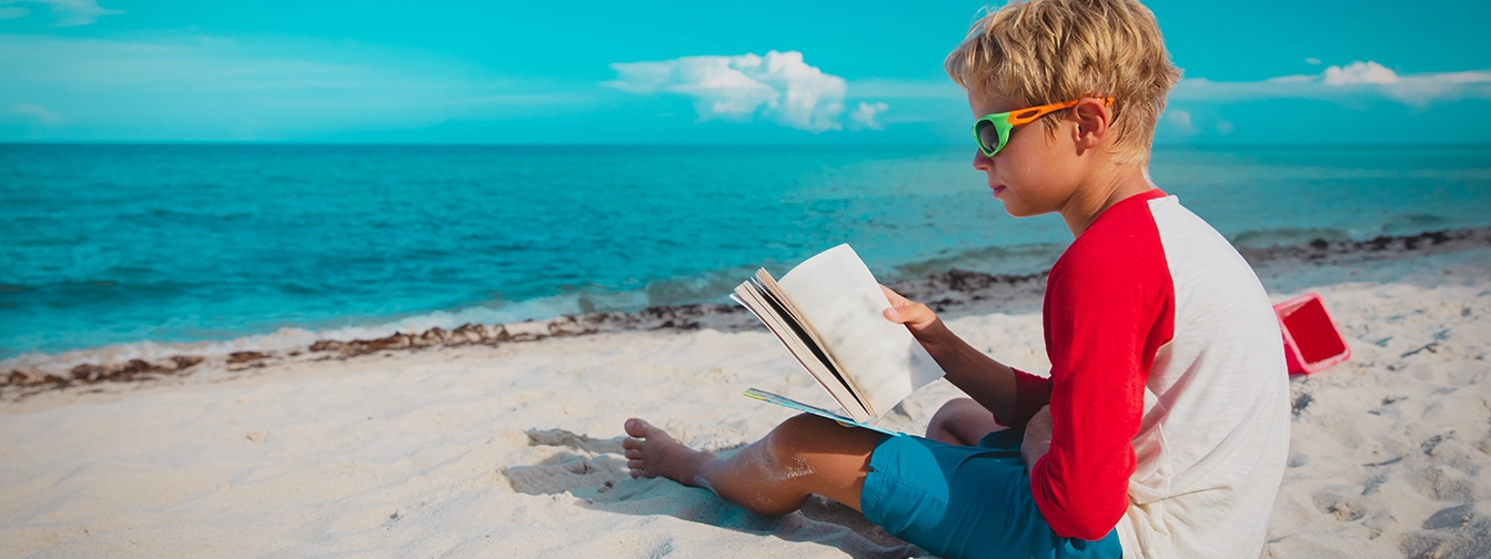 young boy on a beautiful beach reading a book