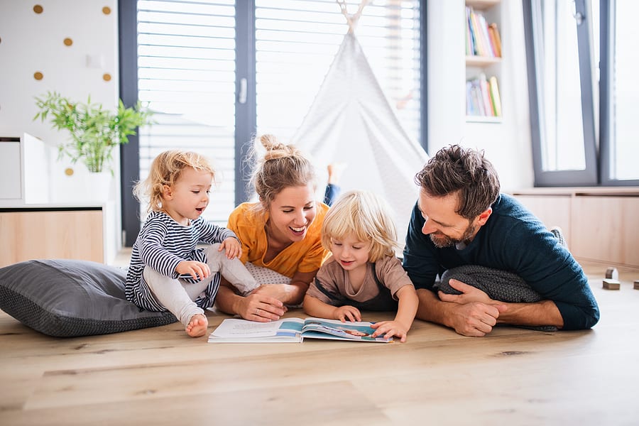 Young family with two small children indoors in bedroom reading a book. Discovery sheet article