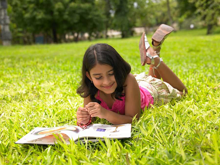Asian girl summer reading in park - Kids Read Now - Summer 2024