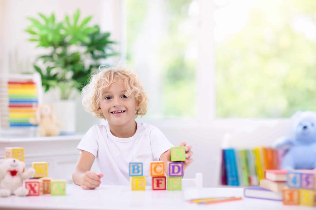 Child learning letters. Kid with wooden abc blocks; home library