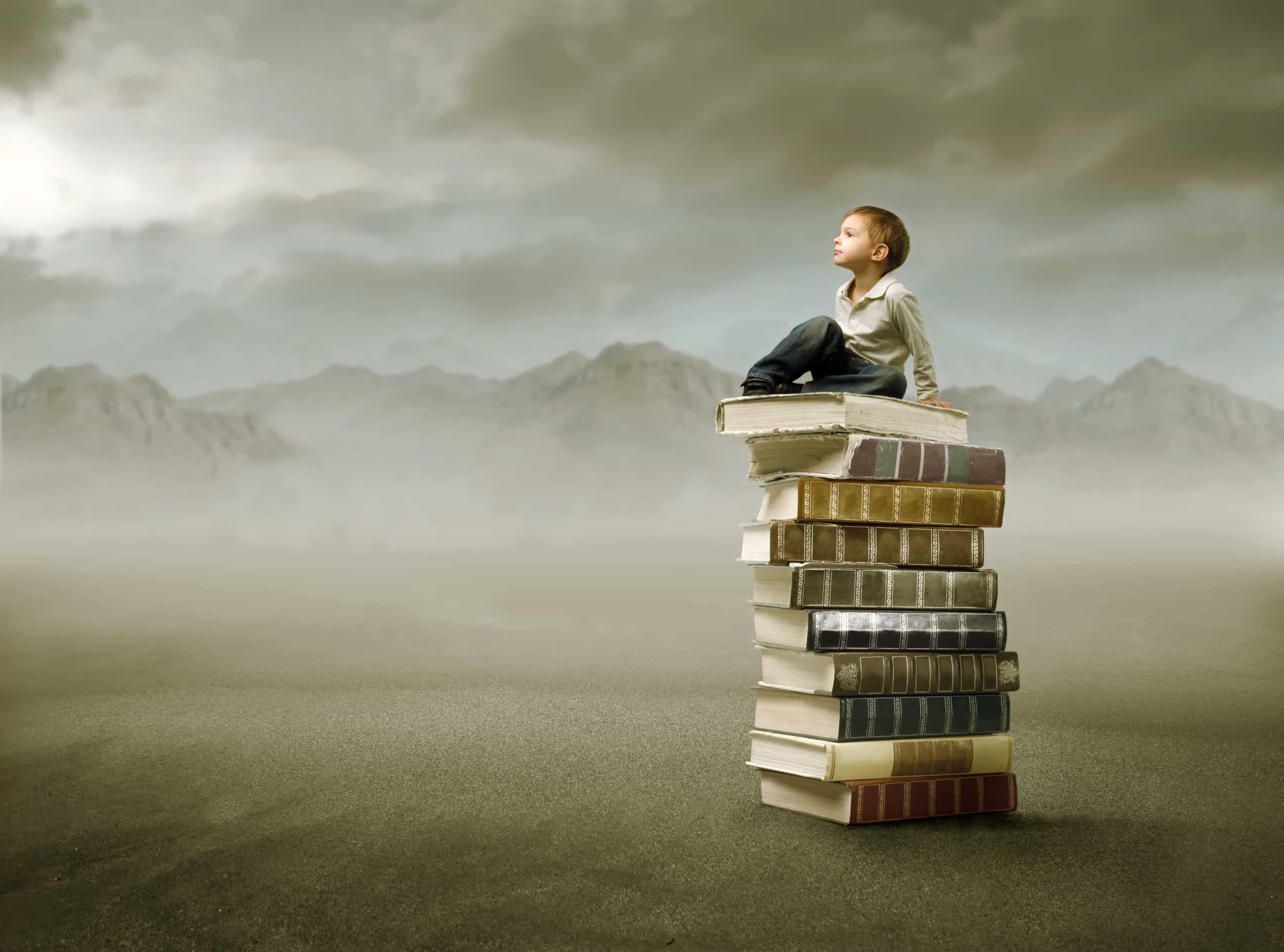 Young boy sitting atop a stack of books